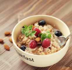 Oatmeal porridge in bowl topped with fresh blueberries and raspberries on wooden table.