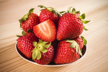 Ripe strawberries in a bowl on a wooden table / Close-up shot of big tasty strawberries lying in bowl on lumber tabletop. Delicious strawberries ready to eat.
