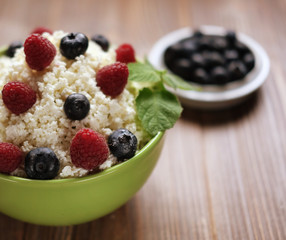 Cottage cheese in green bowl with raspberries and blueberries on wooden background. Healthy Breakfast. Good for diet.