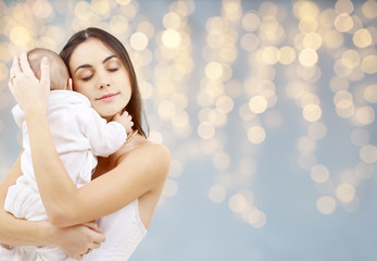 Obraz na płótnie Canvas family and motherhood concept - happy smiling young mother with little baby over festive lights background