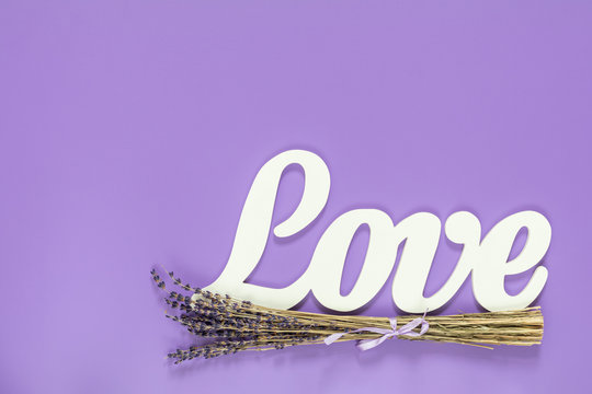 White letters forming word LOVE written with beautiful dried lavender bouquet on violet surface