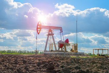 Oil rocking in the field against the cloudy sky with bright sun rays