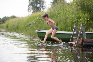 A boy jumping into the water in flight against the backdrop of a rural landscape.