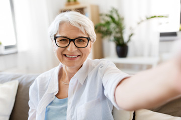 technology, communication and people concept - happy smiling senior woman in glasses taking selfie...