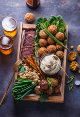 Pastrami, falafel, babagahanoush, veggies and beer in a wooden box, copyspace.
