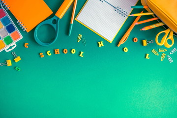 School accessories, pencils, paints, pens on green background. Back to school. Word school, wooden letters. Flat lay, top view, copy space 