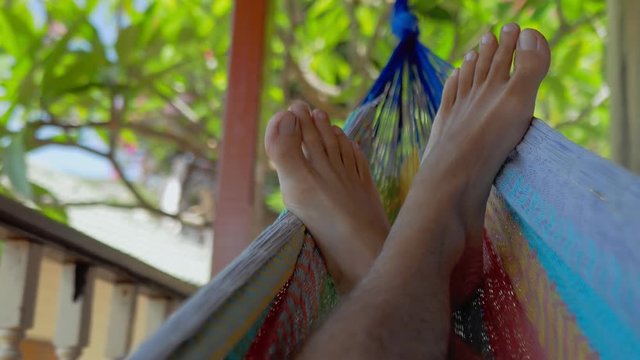 Swinging bare man feets in a hammock on terrace. Vacation on Koh Tao Tanote Bay, Thailand