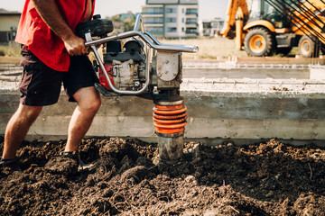 Industrial worker using soil compactor on construction site. Foundation of house details