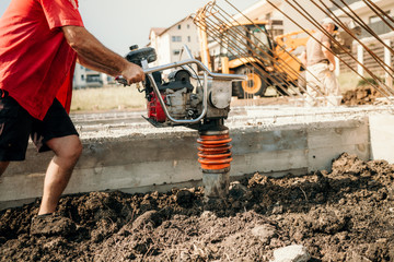 Industrial construction worker compacting soil with vibration compaction machine