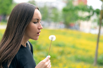 A young woman holding a flowering dandelion in her hand and blowing on a flower