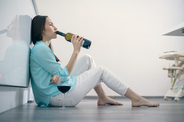 A woman in white jeans and a turquoise shirt sits on the floor in the interior of a white kitchen...