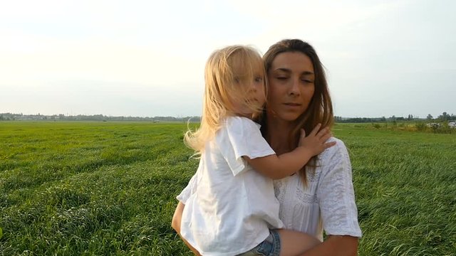 Happy family, mother and her little daughter walk on the green grass, summer evening. Mom with kid walking on green fields. Slow motion