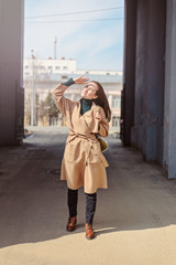 A young woman in a sand coat walks through the arch and looks at the sky, covering her face from the sun