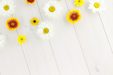 Obraz premium White daisies and garden flowers on a white wooden table. The flowers are arranged in the upper part, the empty space left below.