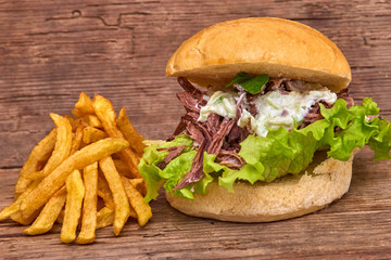 Barbeque Pulled Pork Sandwich with green salad,Tzatziki Sauce,BBQ Sauce and Fries on wooden background