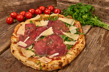 Homemade fresh delicious gourmet pizza whit carpaccio matured beef, rocket and slices of grana cheese,Tasty italian pizza isolated on wooden table,Close up with selective focus