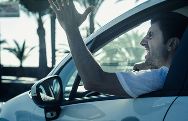 Aggressive man gesticulates with hand out of window while driving. Crazy driver yelling from car on...