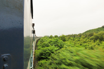 Long blue train crossing jungle in Goa, India. Backpacker, cheap transportation, travel adventure, speed concepts