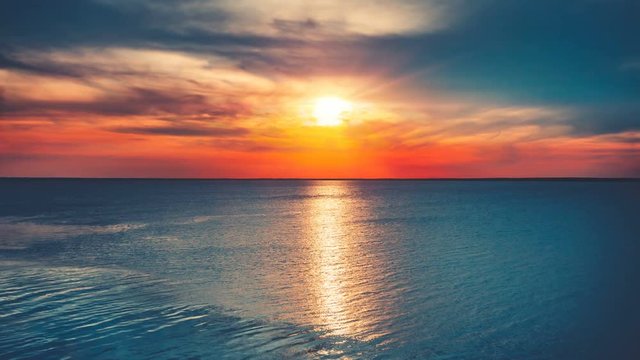 Beautiful sunset over ocean with sun reflection. Bright color toning. Nature landscape. Holidays, travel, vacation. Water waves movement and clouds in sky float. 4K Slow Motion Time Lapse Parallax