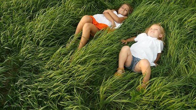 Little girls resting on the green grass. Beautiful kids lying on the field. Cute children dreaming on the nature. Slow motion