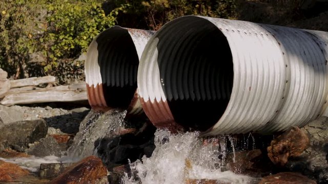 Water Flowing Out Of Rusty Drain Pipes Onto Rocks