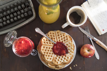 breakfast with waffles and homemade jam on a table with a cup of coffee, lemonade, apple, book and vintage typewriter.