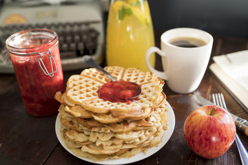 breakfast with waffles and homemade jam on a table with coffee, lemonade, apple and a vintage typewriter