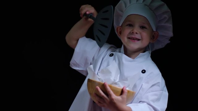 Smily boy wearing chefs suit with bowl of french fries on the black background