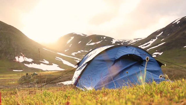 Tent on grass in front of a mountin with snow during sunset. Located in northern Sweden.
