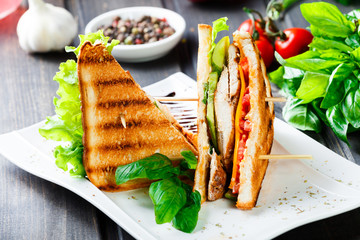 Club sandwich with cheese, cucumber, tomato, chicken meat and lettuce on dark wooden table. Delicious snacks, sandwiches