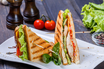 Club sandwich with cheese, cucumber, tomato, chicken meat and lettuce on dark wooden table. Delicious snacks, sandwiches
