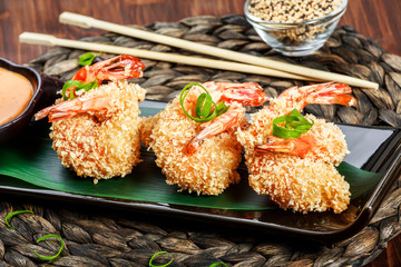 Breaded shrimp with sauce on black plate on bamboo background. Delicious dish of seafood.