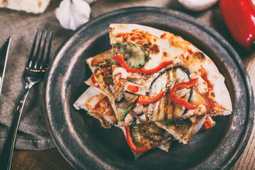 Sliced pizza with chicken, zucchini, eggplant, pepper, cheese and mushrooms on the plate vintage. Top view. Toning.