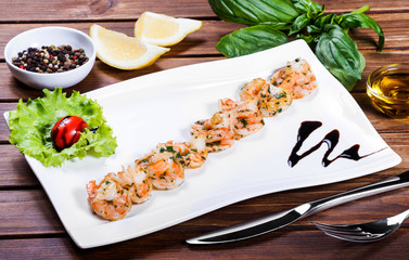 Prawns Shrimps roasted with sauce and greens on white plate on wooden table. Delicious dish of seafood.