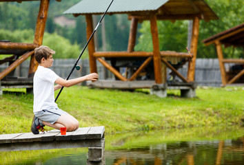  cute boy in white T shirt fishing in the lake and has fun, smiles. vacation with kids, holidays, active weekends concept