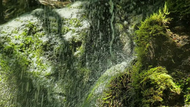 SLOW motion, waterfall in mountains in high speed reel. Closeup of spring water drops falls and splashing on green moss