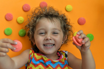Fototapeta na wymiar Little girl on an orange background with a colorful biscuit. Child with a cookie. Girl with a smile