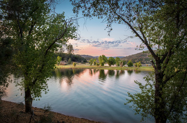 Pink and orange sunset over quiet, mountain lake, framed by leafy trees