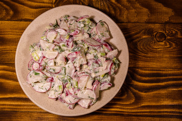 Vegetarian salad with radish, green onion and sour cream on a ceramic plate. Top view