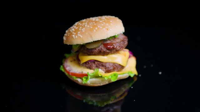 The sesame bun is falling on the top of burger. Slow motion. Black mirror surface