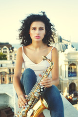 young girl with saxophone on the roof parapet. woman holding a musical wind instrument. young...