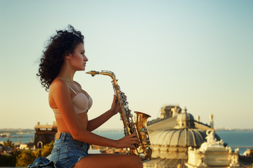 young girl with saxophone on the roof parapet. woman holding a musical wind instrument