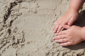 close up of kids hands, touching sand at sea for first time