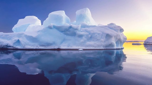 Antarctica Nature. Beautiful blue iceberg with mirror reflection floats in open ocean. Sunset sky in the background. Majestic winter landscape. Travel expedition. Close up. 4K Slow motion Parallax