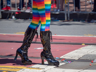 Woman with rainbow tights and high latex boots walking along a street 