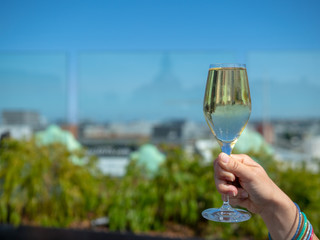 Woman hand holding glass of white wine on a sunny day with city skyline in background