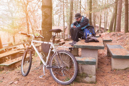 Cyclist with mountain bike and cellphone rests at a picnic area on a cold winter morning. Sport and outdoor activities in nature    
