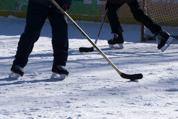 A boy ice hockey amateur player with a stick and a puck on ice. Feet in hockey skates and a stick...