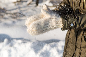 Portrait of a beautiful brunette girl playing with snow in winter forest. Woman in white knitted hat and mittens. Christmas girl winter woman shakes off white snow from her hands.