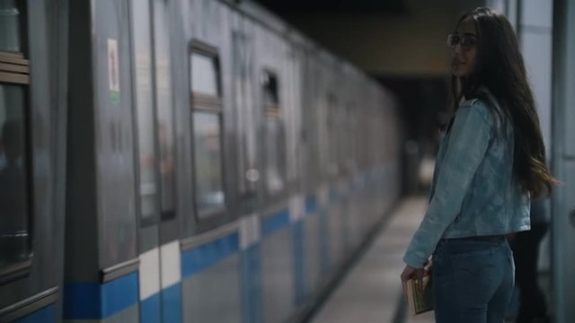 Girl looks around, standing on the platform, passing train, slow motion